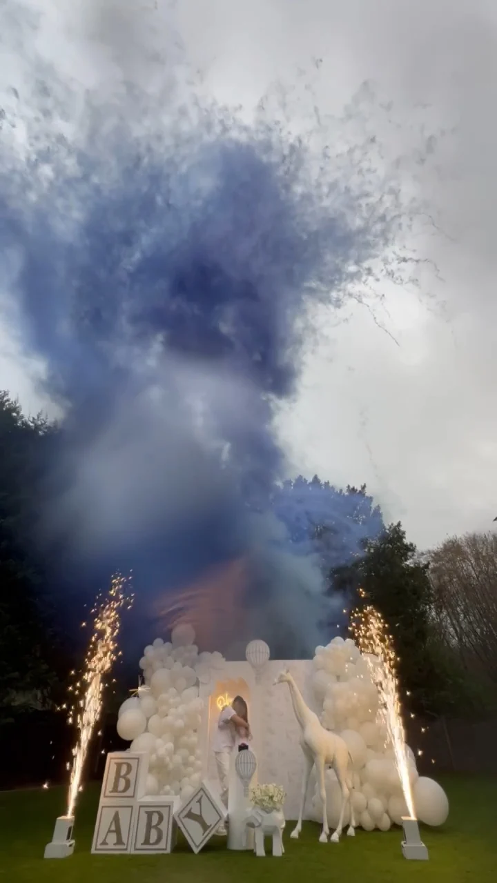 A blue smoke canopy above a balloon backdrop, with spark fountains framing the reveal. Illustrative reveal footage; effects vary by package.