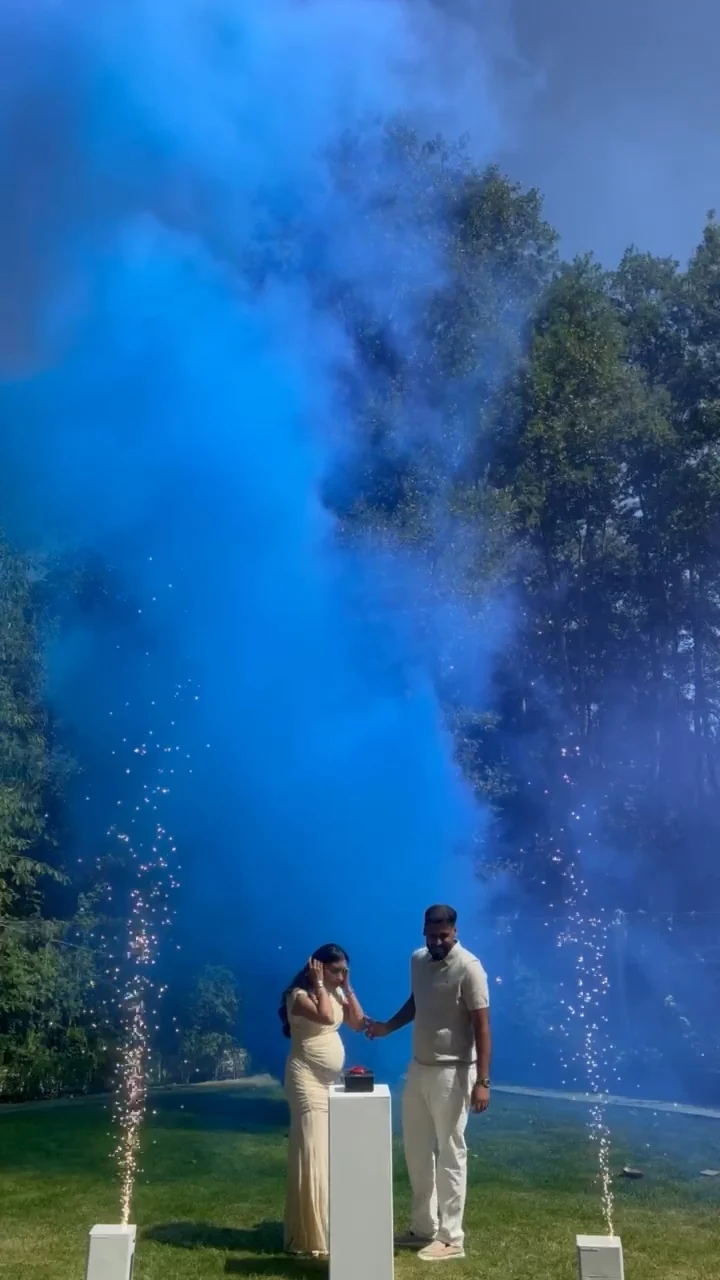 A tall blue smoke cloud rises over a sunny garden as the couple celebrate. Illustrative reveal footage; effects vary by package.